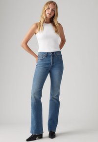 Blå jeans med en utsvängd form, tillverkade av denim. Har hög midja, femfickorsdesign och en mjuk, lätt textur. Tillsammans med en vit linne.