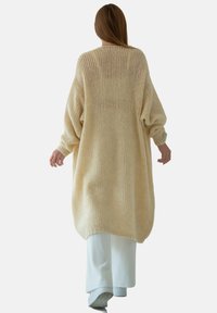 Beżowy, oversize'owy sweter z dzianiny z długimi rękawami i luźnym krojem, z wyraźnym wzorem i szerokim, okrągłym dołem.