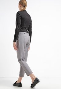 Camisa negra ajustada de manga larga, pantalones grises a medida y zapatos negros. Los pantalones tienen bolsillos traseros y dobladillos con puños.