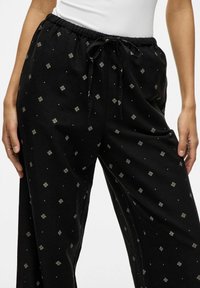 Pantaloni del pigiama neri con cintura elastica e cordino, decorati con motivi geometrici bianchi e un tessuto morbido e texture.