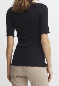 Black ribbed short-sleeve top with a scalloped hem, fitted design, and a soft texture, paired with beige fitted trousers.