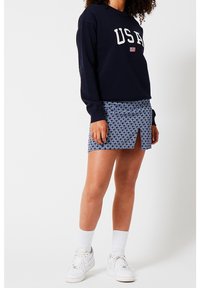 Marinblå sweatshirt med "USA"-text, mönstrad kjol i blått och vitt med en framtida slits, matchad med vita sneakers och strumpor.