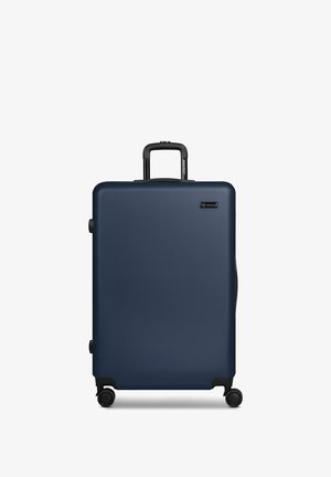 Maleta rígida azul marino con cuatro ruedas y un asa extensible negra, de pie sobre un fondo blanco.