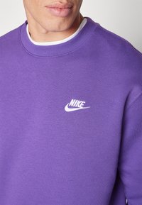 Lila sweatshirt med rund halsringning, tillverkad av mjukt tyg. Har en vit Nike-logotyp på bröstet. Enkel, ren design.