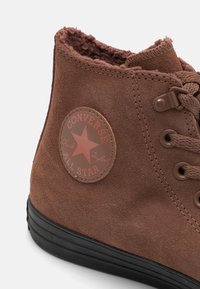 Tenis brown din suede, cu guler înalt, cu un finisaj texturat, talpă din cauciuc negru și un logo circular care conține o stea și numele brandului pe partea laterală.