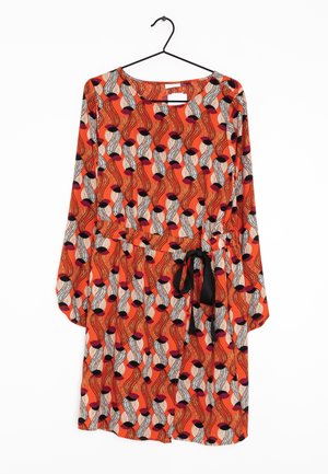 Robe orange à manches longues avec un motif ondulé abstrait en noir, blanc et violet, et une ceinture noire à la taille, suspendue à un cintre noir.