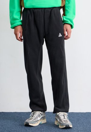 Pantaloni de jogger din fleece negru cu talie elastică și buzunare laterale, având un mic logo triunghiular alb pe parte stângă a coapsei.