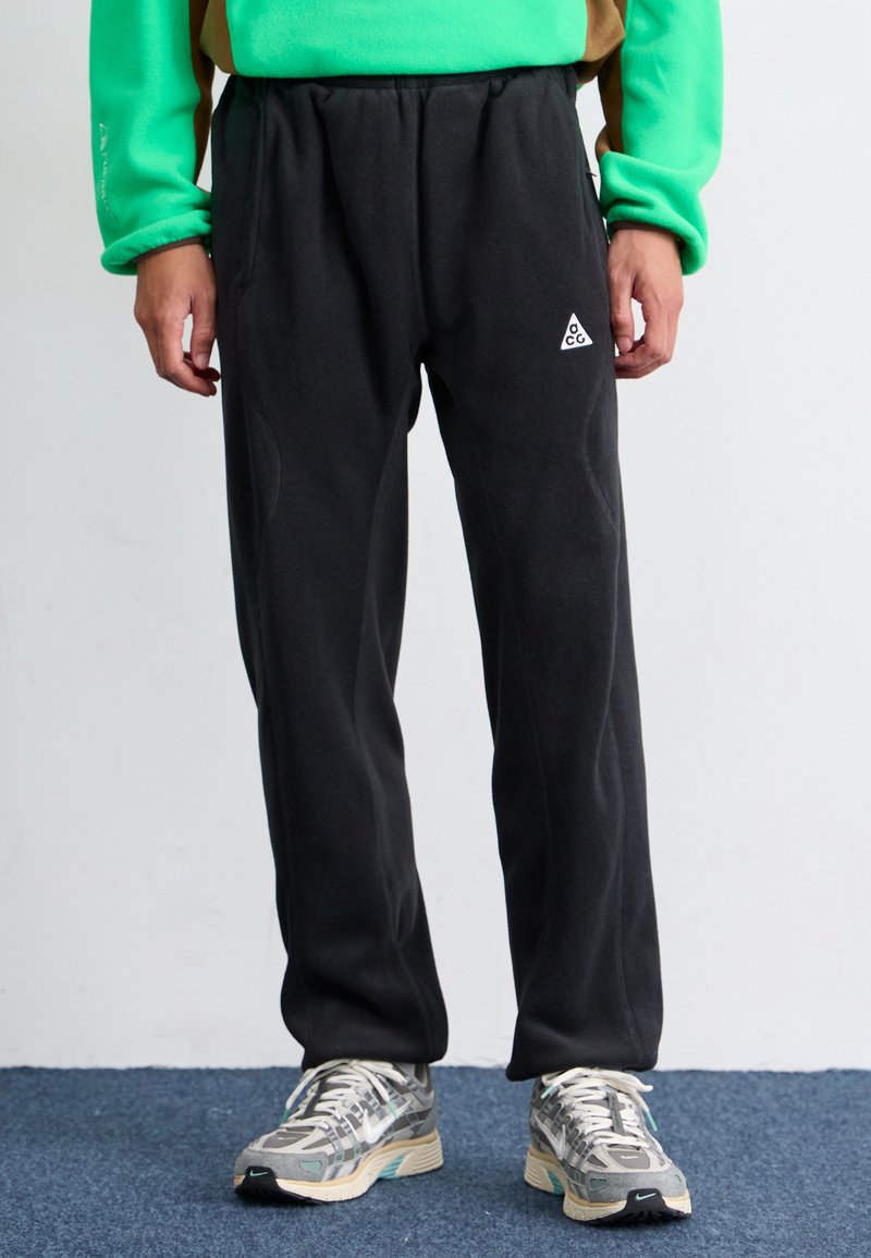 Black fleece joggers with an elastic waistband and side pockets, featuring a small white triangular logo on the left thigh.