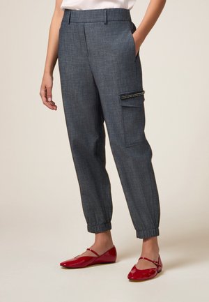 Pantaloni grigi a sigaretta realizzati in tessuto intrecciato, con tasca laterale con hardware decorativo e polsini elasticizzati. Abbinati a ballerine rosse.