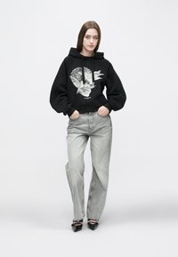 Μαύρο κοντό φούτερ με γραφικό σχέδιο, γκρι τζιν ψηλόμεσο, και μαύρες ψηλοτάκουνες γόβες με διακοσμητικές λεπτομέρειες στη λουρίδα.