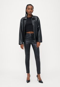 Svart skinnjakke med glidelås over en svart crop top, kombinert med skinnende svarte skinny jeans og svarte stiletthæler, som skaper en strømlinjeformet silhuett.