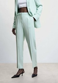 Mintgroene op maat gemaakte blazer en broek, met strakke lijnen, plooien en puntige zwarte hakken, wat een moderne, samenhangende uitstraling creëert.