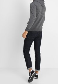 Grijze hooded sweatshirt met een getailleerd ontwerp, gecombineerd met donkere denim jeans met opgerolde mouwen en zwarte sneakers met witte accenten.