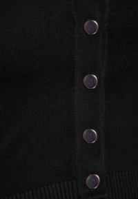Cardigan negru din tricot cu nervuri, cu închidere prin butoane metalice pe partea frontală. Textura este netedă, având un design ajustat și o întindere subtilă.