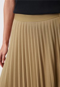 Jupe plissée en tissu kaki avec une taille côtelée. Comprend des plis verticaux pour une texture et une silhouette fluide.