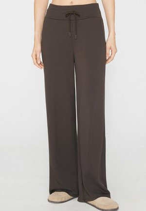 Braune Hose mit weitem Bein und Kordelzug in der Taille, getragen mit beigen Hausschuhen, gezeigt von der Taille bis zu den Füßen einer stehenden Person.
