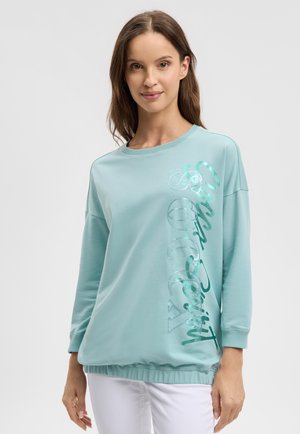 Light blue sweatshirt with a round neckline, long sleeves, and a cropped fit. Features shiny text design along the left side.