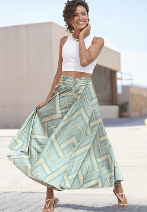 Maxi rok in lichtteal stof, met een geometrisch patroon in blauw en geel. Gecombineerd met een witte crop top en gouden sandalen.