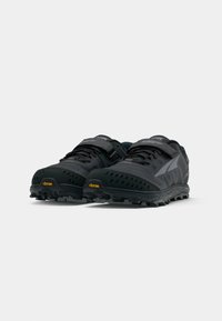 Black trail running shoes with a textured upper, Velcro strap, and Vibram outsole. Features a low-profile design and multiple ventilation holes.