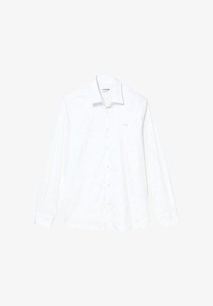 Balta krekls ar garām piedurknēm un pogām pie apkakles, izgatavots no viegla auduma. Uz kreisā krūts ir neliels, tonāls logotips.