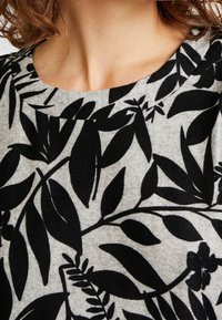 Haut en tissu gris avec un motif floral noir comprenant des feuilles et de petites fleurs. Encolure ronde, texture douce et poids moyen.