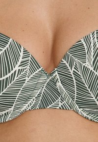 Top bikini verde con motivo a foglie bianco. Presenta una texture liscia e un design a scollo profondo con hardware centrale.