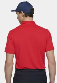 Rode polo shirt met korte mouwen en een textuurafwerking, voorzien van een klassieke kraag. Gecombineerd met donkere broek en een marineblauwe pet.