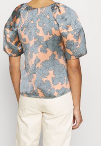 Korte mouw blouse in pastelroze met grote blauwe bloemenprint. Heeft geplooide pofmouwen en een ronde hals. Zachte stoftextuur.