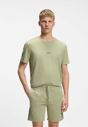 Ung mand iført lysegrøn BOSS t-shirt og matchende shorts står med den ene hånd i lommen mod en hvid baggrund.