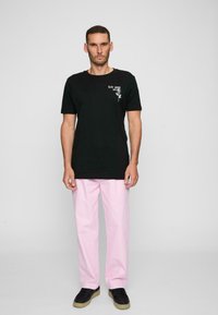 Černé bavlněné tričko s bílým grafickým textem a designem růže, spárované s světle růžovými kalhotami a černými teniskami. Minimalistický styl.