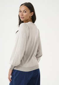 Pull en tricot gris clair avec un col rond, des manches longues bouffantes et un ourlet côtelé. Porté avec un pantalon en denim bleu.