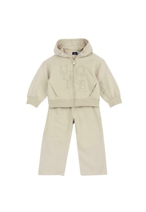 Ensemble enfant beige deux pièces avec veste à capuche zippée avec lettres embossées et pantalon large assorti.