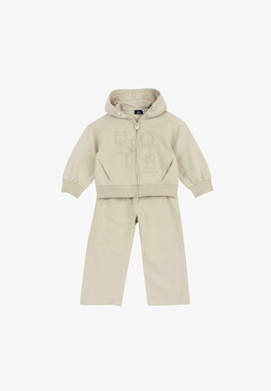Ensemble enfant beige deux pièces avec veste à capuche zippée avec lettres embossées et pantalon large assorti.