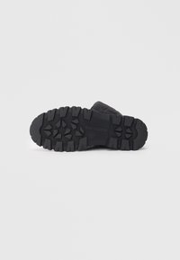 Black rubber boot sole featuring a textured, rugged pattern for traction, with embossed branding in the center and reinforced edges.