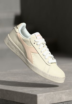 Basket en cuir crème avec des accents rose clair, lacets blancs, détails perforés et semelle texturée. Logo sur la languette.