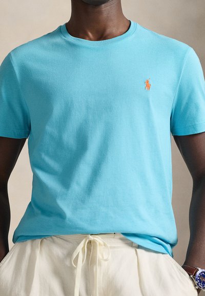 Ανοιχτό μπλε βαμβακερό μπλουζάκι με στρογγυλή λαιμόκοψη και κοντά μανίκια. Διαθέτει πορτοκαλί κεντημένο λογότυπο στο αριστερό στήθος. Λεία υφή.