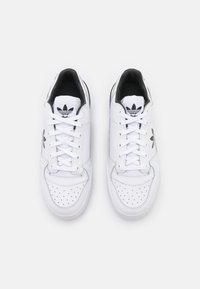 White leather sneakers with black accents, perforated toe box, padded tongue, and laces, featuring a black logo near the heel.