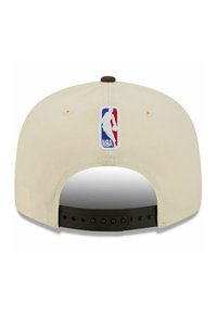 Cremefarbene Baseballkappe mit schwarzem Snapback-Verschluss. Auf der Rückseite ist ein gesticktes NBA-Logo in Rot, Weiß und Blau angebracht.