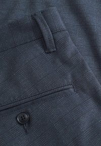 Pantaloni color blu navy scuro con una tessitura strutturata, dotati di una tasca posteriore e chiusura con bottone. Il tessuto presenta un sottile motivo a quadri.