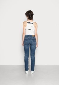 Top de alças branco com padrão de tie-dye preto, combinado com jeans skinny azul-escuro e sapatilhas brancas, visto de costas.