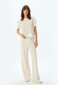 Lichte gebreide top in off-white met raglanmouwen over een wit T-shirt, gecombineerd met luchtige, crèmekleurige wijde broeken.
