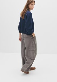 Felpa blu navy con spalle scese e polsini a costine, abbinata a pantaloni cargo grigio chiaro a gamba larga con tasche grandi. Scarpe marroni.
