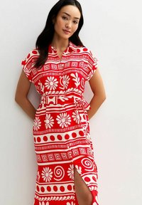 Vestido rojo con patrones florales y geométricos en blanco, mangas cortas, botones al frente, cintura ajustada con un lazo y abertura lateral para mayor comodidad al moverse.