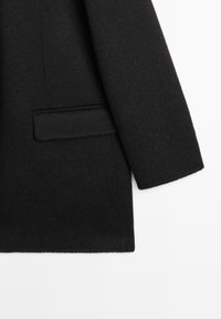 Cappotto di lana nero con una texture liscia, tasca singola sul petto e vestibilità su misura con un classico design a rever.
