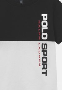 Cotton t-shirt with a black top half and white bottom half, featuring bold black and red text: "POLO SPORT RALPH LAUREN" on the side.