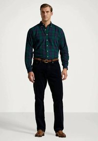 Green and navy plaid button-up shirt, paired with dark pants and a brown belt, featuring a classic collar and chest pocket.