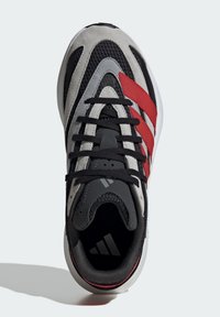 Čierne a sivé atletické tenisky s červenými pruhmi Adidas, s prvkom z mrežovanej tkaniny a šnúrkovaním na vrchu. Zaoblená špička a polstrovaný golier.