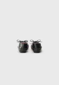 Pantofi din piele neagră cu un design rotund, având fundițe mici la spate și texturănetedă. Talpa este plată, cu o minimă ridicare.