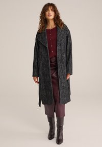 Plašč v črno-beli ribji kost podobi z velikimi ovratniki in stranskimi žepi, oblečen čez maroonski pleteni top in rjav usnjen krilo.