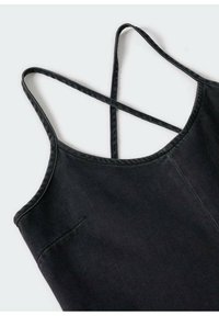 Top de denim negro con tirantes delgados ajustables, con escote en forma de scoop, diseño de espalda cruzada y un bolsillo lateral. Textura suave.